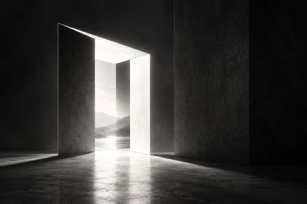 A tall doorway in a dark concrete room, light falling through it onto the floor, mountains and still water beyond